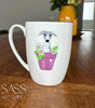 White mug with a dog illustration in a pot of flowers on a wooden table, featuring 'SASS Artworks' branding.
