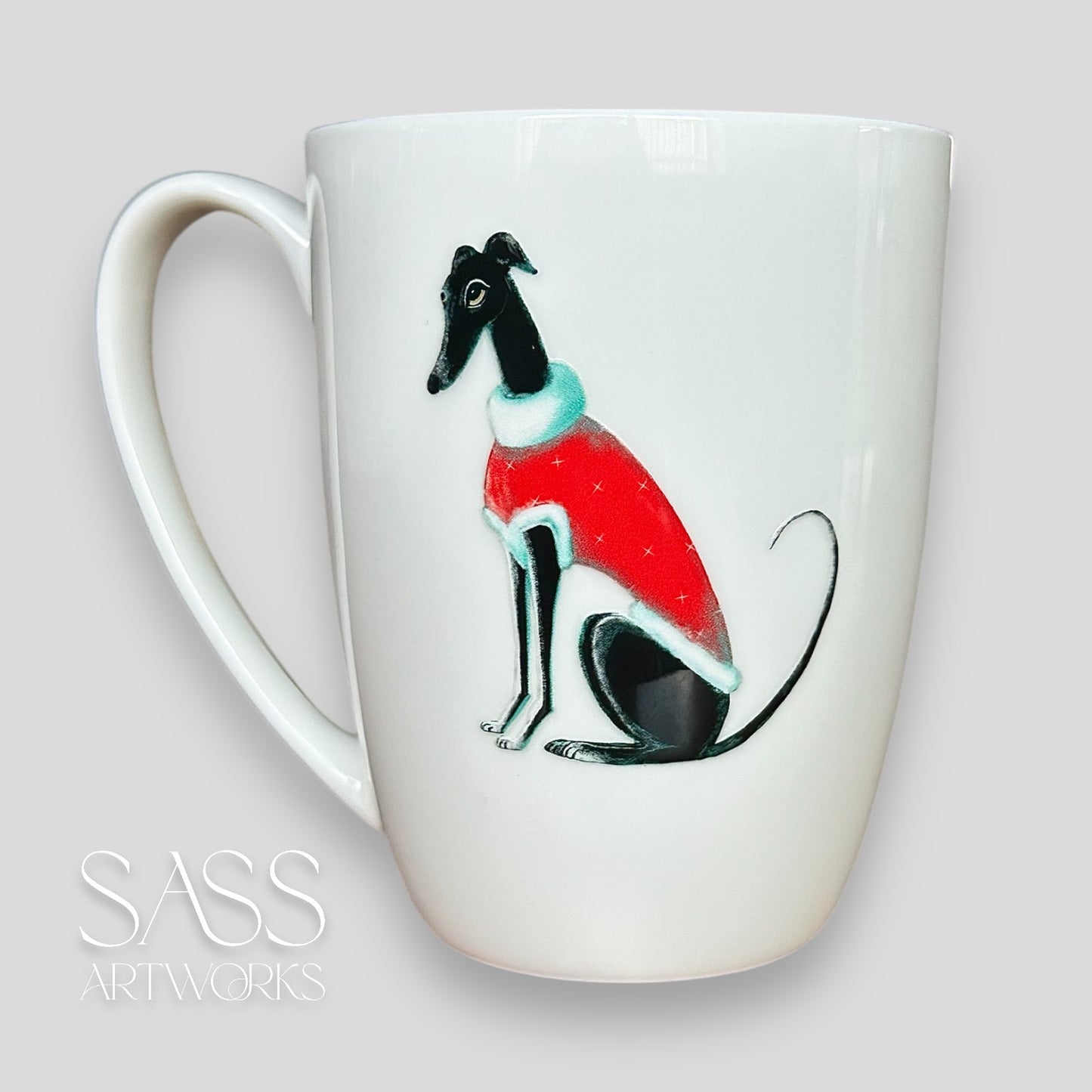 White mug with a black greyhound or whippet wearing a red sweater design on a light gray background, featuring 'SASS Artworks' branding.