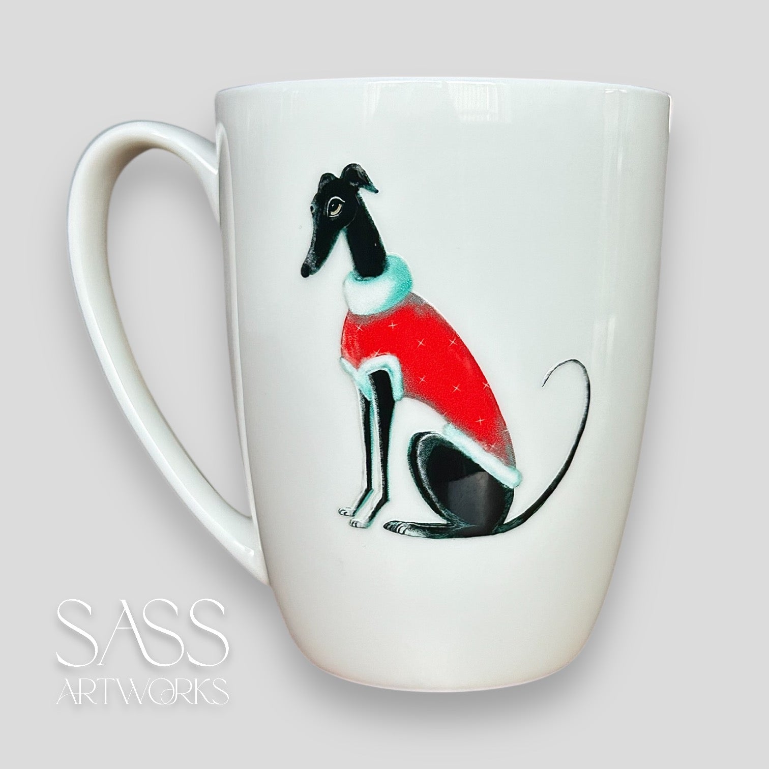 White mug with a black greyhound or whippet wearing a red sweater design on a light gray background, featuring 'SASS Artworks' branding.