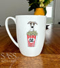 White mug with a whippet and popcorn design on a wooden table, featuring 'SASS Artworks' branding.