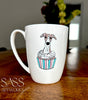 White mug with a whippet  in a cupcake design on a wooden surface, featuring 'SASS Artworks' branding.