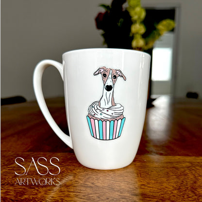 White mug with a whippet  in a cupcake design on a wooden surface, featuring 'SASS Artworks' branding.