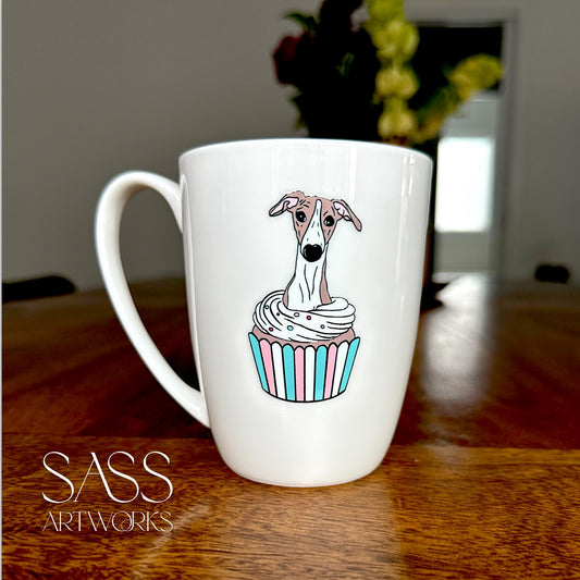 White mug with a whippet  in a cupcake design on a wooden surface, featuring 'SASS Artworks' branding.