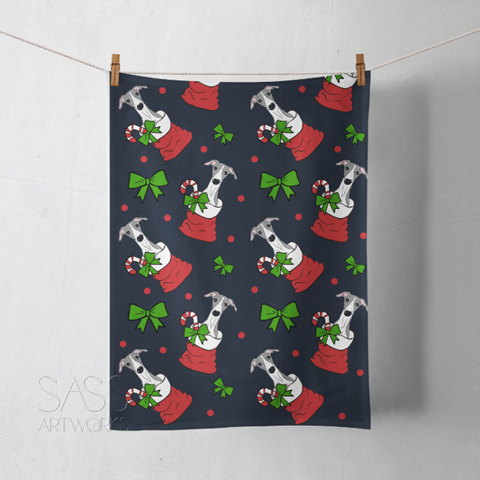 Festive towel with Christmas-themed pattern of whippets or greyhounds in red sacks, candy canes, and bows on an ink blue background.