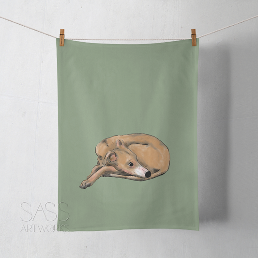 Green tea towel with a whippet illustration hanging on a line against a white wall.